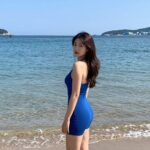 여름 블루 원피스 스타일링과 활용법 여름 해변에서 푸른 바다를 배경으로 블루 원피스를 입은 여성이 자연스럽게 포즈를 취하고 있다