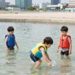 아이 물놀이 안전 준비 핵심 용품 어린이 물놀이 용품 아쿠아슈즈와 구명조끼를 착용한 아이가 물놀이를 즐기는 모습