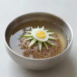 집에서 만드는 냉면 재료 준비 완성 비법 집에서 만든 물냉면 완성 그릇, 오이와 달걀 고명, 육수 위에 냉면 다대기 올려져 있음