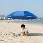 유아 파라솔 세트 선택과 사용 꿀팁 해변에 설치된 유아 파라솔 세트 아래 아이가 장난감을 가지고 노는 모습